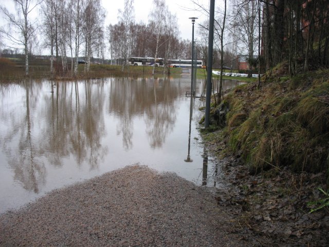 Kävelytie tulvaveden alla, taustalla busseja tiellä.