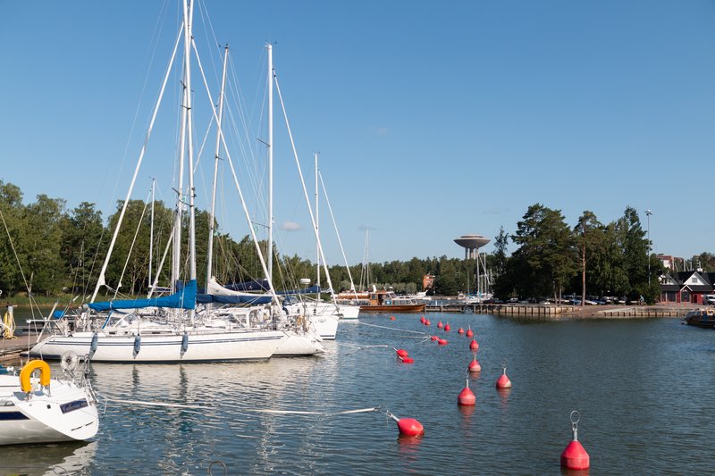 Purjeveneitä satamassa aurinkoisena kesäpäivänä, taustalla vesitorni.
