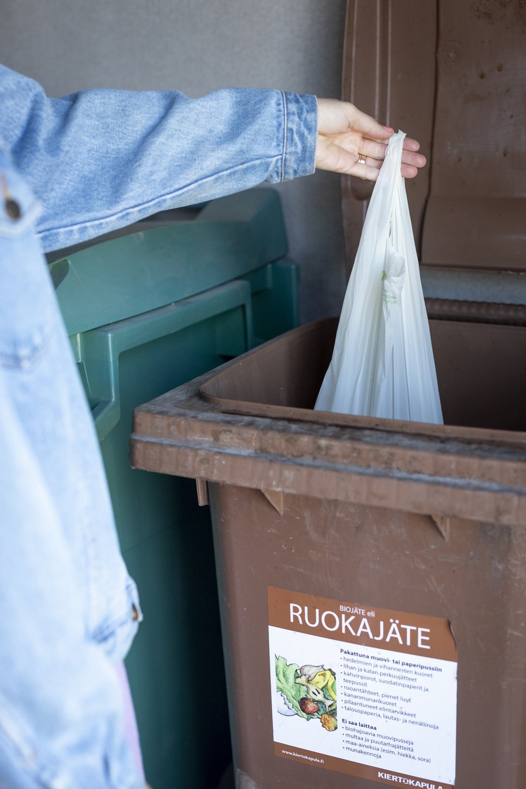 Käsi, joka laskee biojätepussin biojäteastiaan.