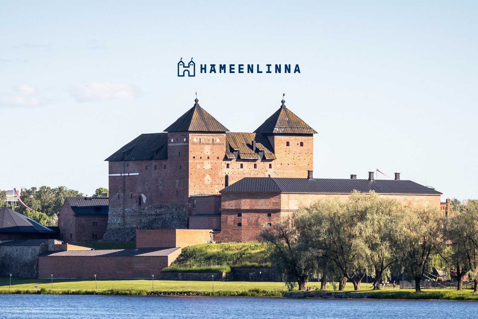 Hämeen linna, puita ja vettä, vaaleansininen taivas.