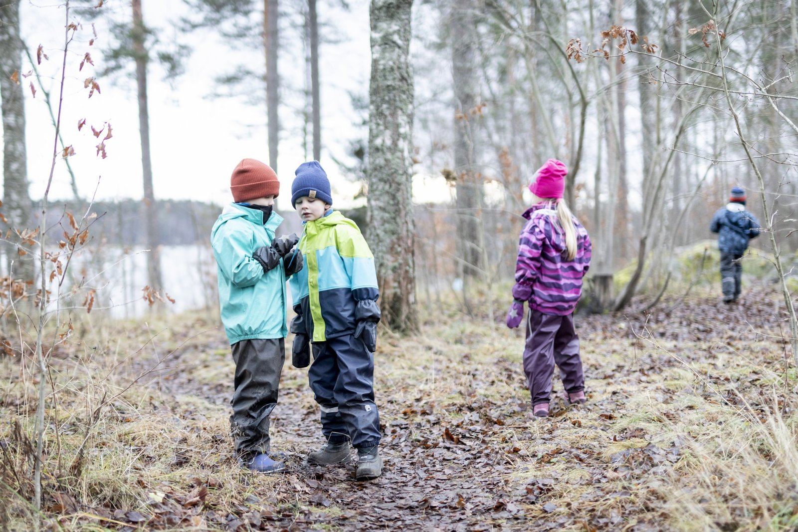 Lapsia syksyisessä metsässä, takana vesialue.