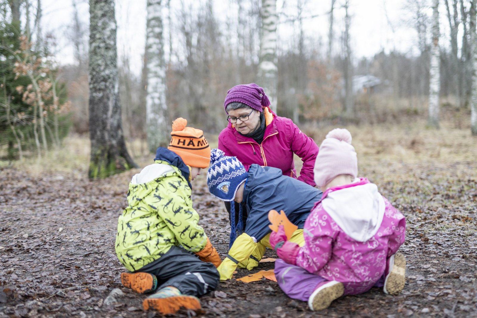 Kolme lasta ja aikuinen tutkii ulkona maata.