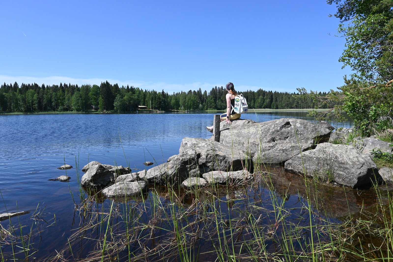 Henkilö istumassa veden äärellä reppu selässä.