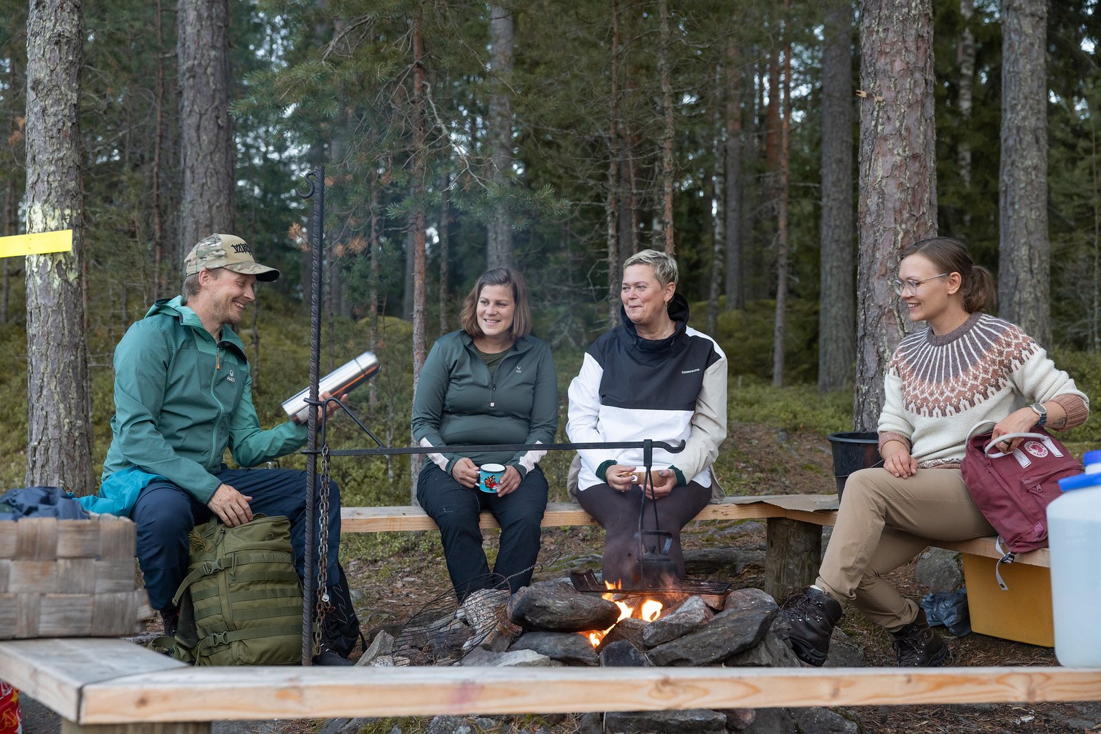 Neljä ihmistä nuotiolla, yhdellä termospullo kädessä.